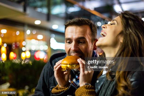 happy couple eating fast food together - couple face to face stock pictures, royalty-free photos & images