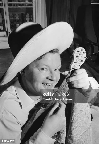 English comedian Benny Hill strums a ukulele at home, 24th April 1965.
