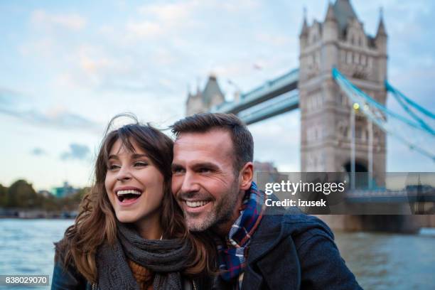 glimlachend paar staande tegen tower bridge london - couple london stockfoto's en -beelden