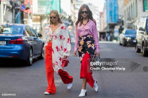 Emili Sindlev wearing a blouse, red flared pants outside iis Woodling and Darja Barannik wearing a skirt with floral print, pink blouse, grey...