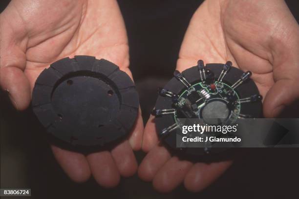 Close-up of a pair of hands that hold the two opened halves and electronic center of a FoxTrax, a specialized, illuminated ice hockey puck used in...