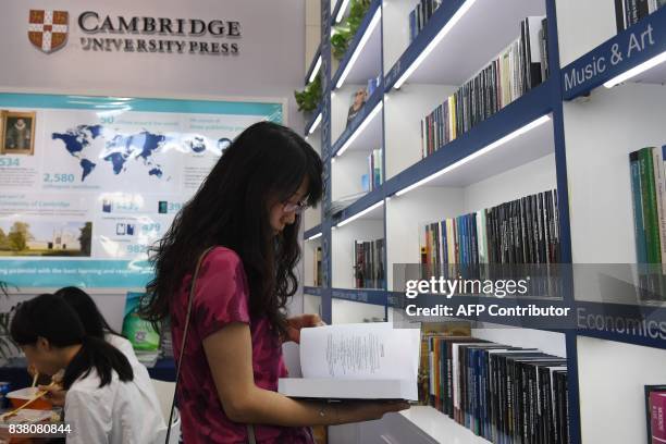 This photo taken on August 23, 2017 shows a woman reading a book at the Cambridge University Press stand at the Beijing International Book Fair in...