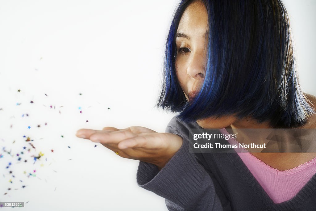 Young woman blowing confetti from hand