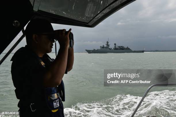 Member of the Malaysian Maritime Enforcement Agency officer uses a pair of binoculars to scan the sea as Royal Malaysian Navy war ship "KD Lekui"...