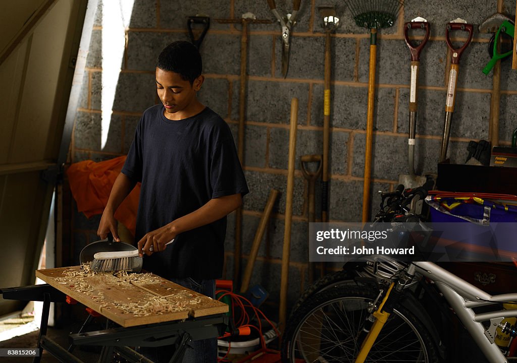 Teenager sweeping up sawdust on workbench