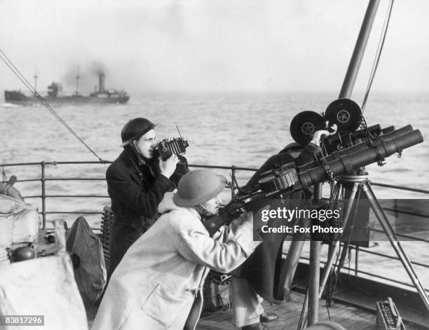 Film and still cameramen alongside a machine-gunner on board a British naval convoy vessel, circa 1942.