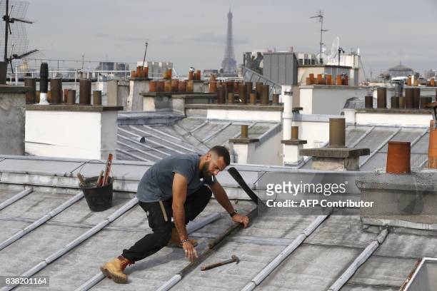 Un French roofer works on August 24, 2017 on a zinc roof of a Paris' building with, in background, the Eiffel tower. / AFP PHOTO / PATRICK KOVARIK