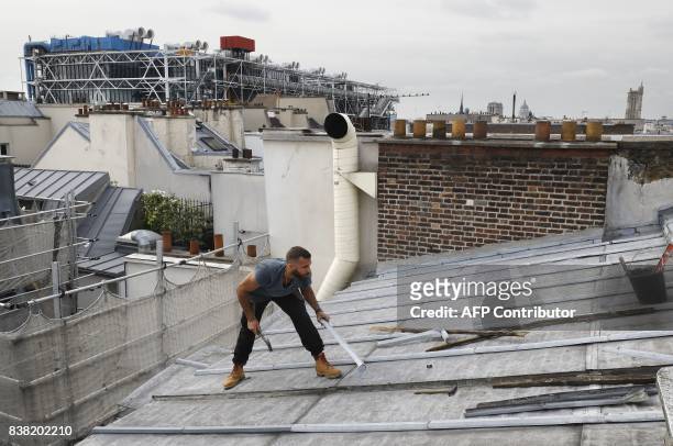 Un French roofer works on August 24, 2017 on a zinc roof of a Paris' building with, in background, the Centre Georges Pompidou museum. / AFP PHOTO /...