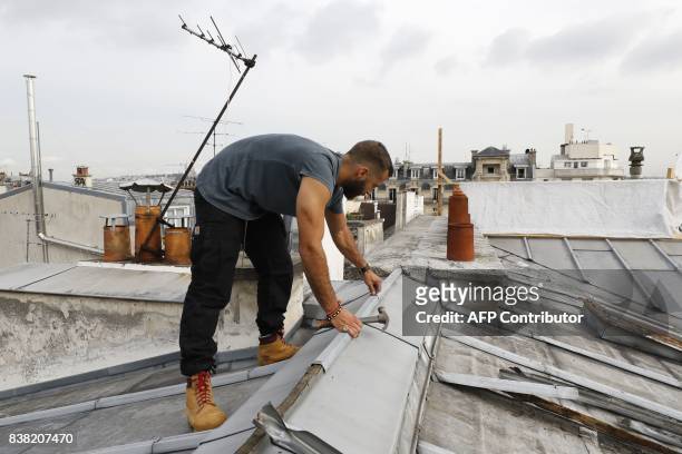Un French roofer works on August 24, 2017 on a zinc roof of a Paris' building. / AFP PHOTO / PATRICK KOVARIK