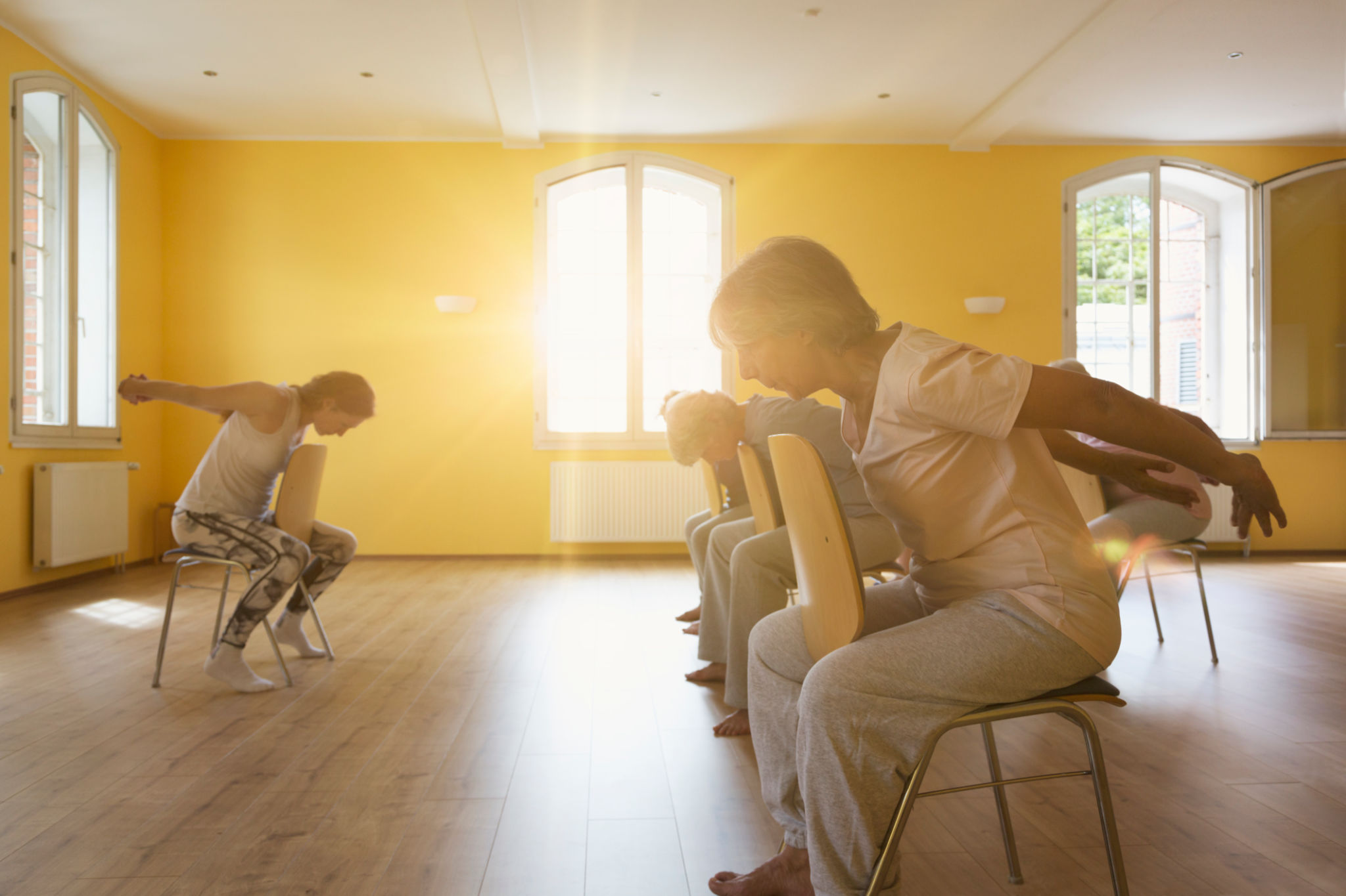 Teacher and active senior women doing yoga class on chairs Teacher and active senior women doing yoga class on chairs