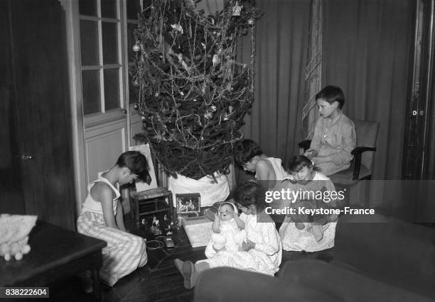Enfants ouvrant leurs cadeaux sous le sapin de Noël, à Paris, France le 25 décembre 1950.