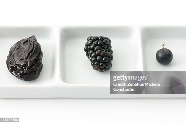 prune, blackberry and blueberry on dish with compartments - dörrpflaume stock-fotos und bilder