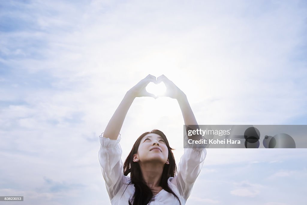 A woman making a heart by hands under a sky