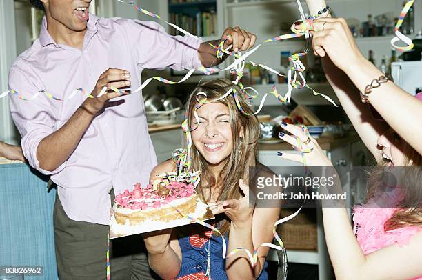 friends throwing streamers over woman holding cake - birthday stockfoto's en -beelden