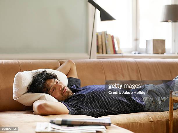 young man lying on sofa watching tv - sofa photos et images de collection