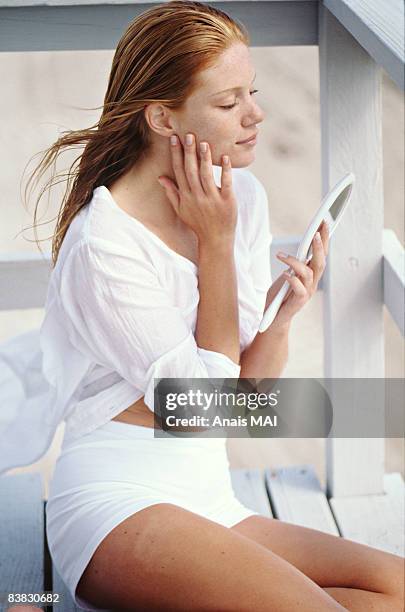 young woman sitting on a balcony, looking at herself in a mirror - beach hair stock-fotos und bilder