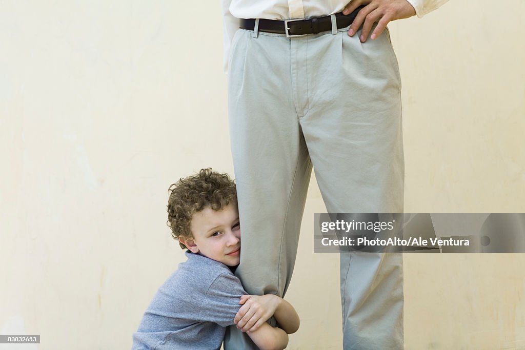 Boy clinging to his father's leg, looking at camera, cropped view