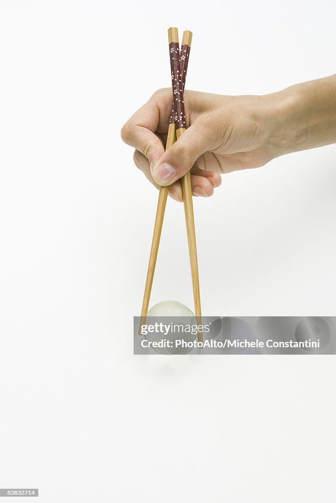 Hands using chopsticks to hold transparent globe, cropped view