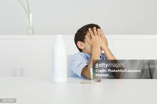 boy with spilled milk, covering face with hands - spilt milk foto e immagini stock