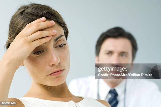 woman holding head, looking down, doctor in background - doctor looking down stock pictures, royalty-free photos & images