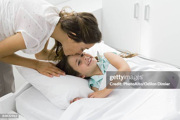 girl lying in bed, mother bending over to kiss her forehead - good night kiss - fotografias e filmes do acervo