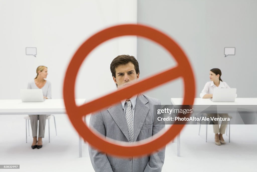 Warning sign across businessman in office, two women sitting with laptops in background