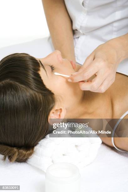 woman lying on back, beautician rubbing cotton swab under her eye - augenlid stock-fotos und bilder