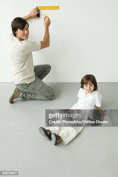 man measuring wall with a ruler, son sitting nearby, both smiling at camera - set square stock pictures, royalty-free photos & images