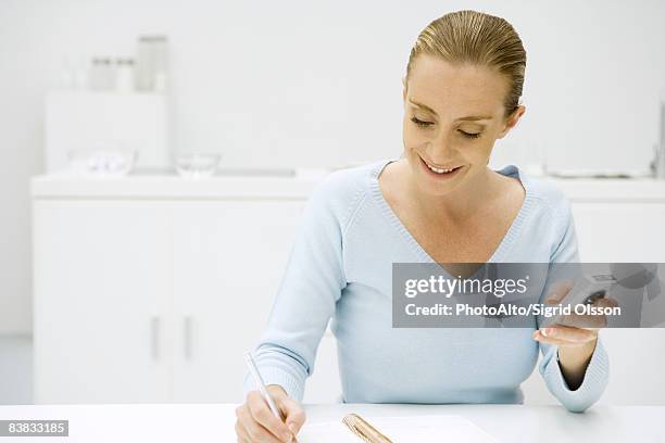 woman writing in notebook and holding cell phone - dictaphone stock pictures, royalty-free photos & images