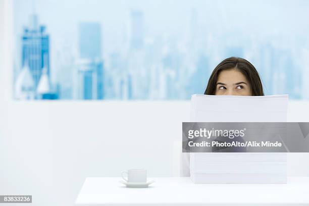 woman sitting behind stack of paper, looking over and away - reserved stock pictures, royalty-free photos & images