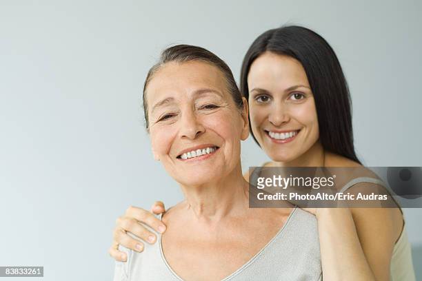 woman behind senior mother, hands on shoulders, both smiling at camera, portrait - old man young woman stock-fotos und bilder