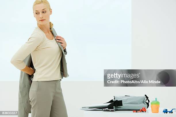 professional woman dressing, looking over shoulder, sippy cup and toys next to bag - businesswoman in suit jackets stock-fotos und bilder