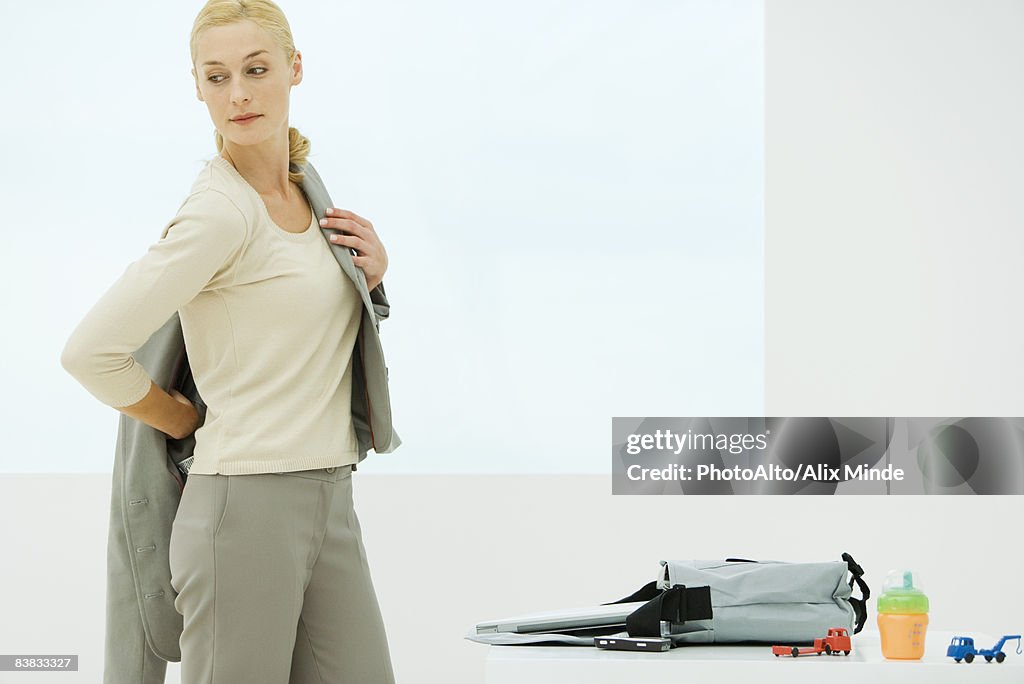 Professional woman dressing, looking over shoulder, sippy cup and toys next to bag