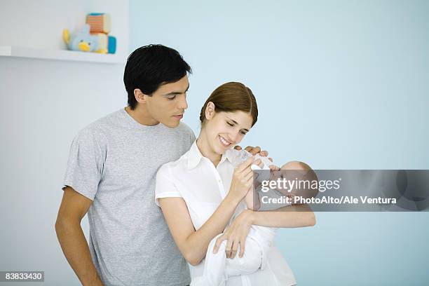 mother feeding baby with a bottle, huband watching over her shoulder - young couple with baby stock pictures, royalty-free photos & images