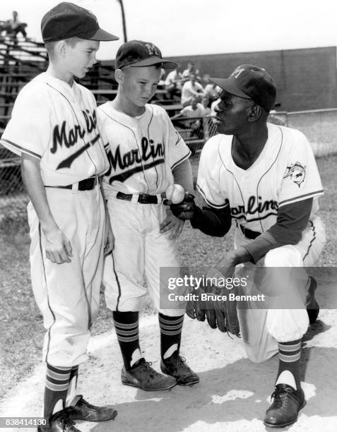 Pitcher Satchel Paige of the Miami Marlins of the International League shows the club's batboy Chet Fields and clubhouse boy Bobby Porter how to hold...