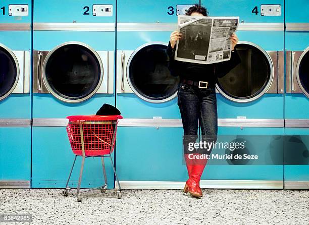 woman reading at laundromat - waschsalon stock-fotos und bilder