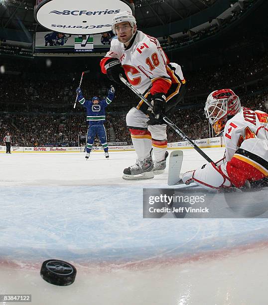 Matthew Lombardi of the Calgary Flames watches the puck get by teammate Miikka Kiprusoff while Jannik Hansen of the Vancouver Canucks celebrates the...