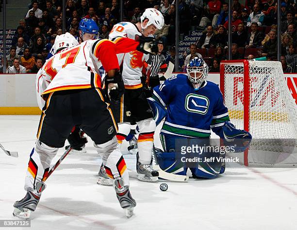 Curtis Sanford of the Vancouver Canucks watches a loose puck near his crease with Curtis McElhinney of the Calgary Flames and teammate Rene Bourque...