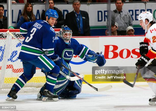 Curtis Sanford and Kevin Bieksa of the Vancouver Canucks and Curtis Glencross of the Calgary Flames look for a rebound during their game at General...