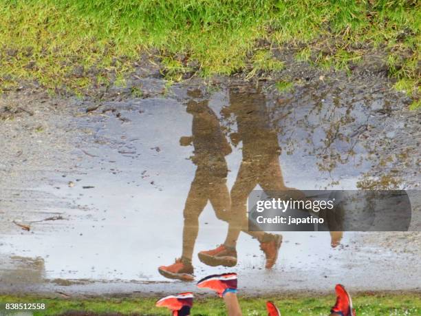 two male athletes running reflected in a puddle of water - male feet stock-fotos und bilder