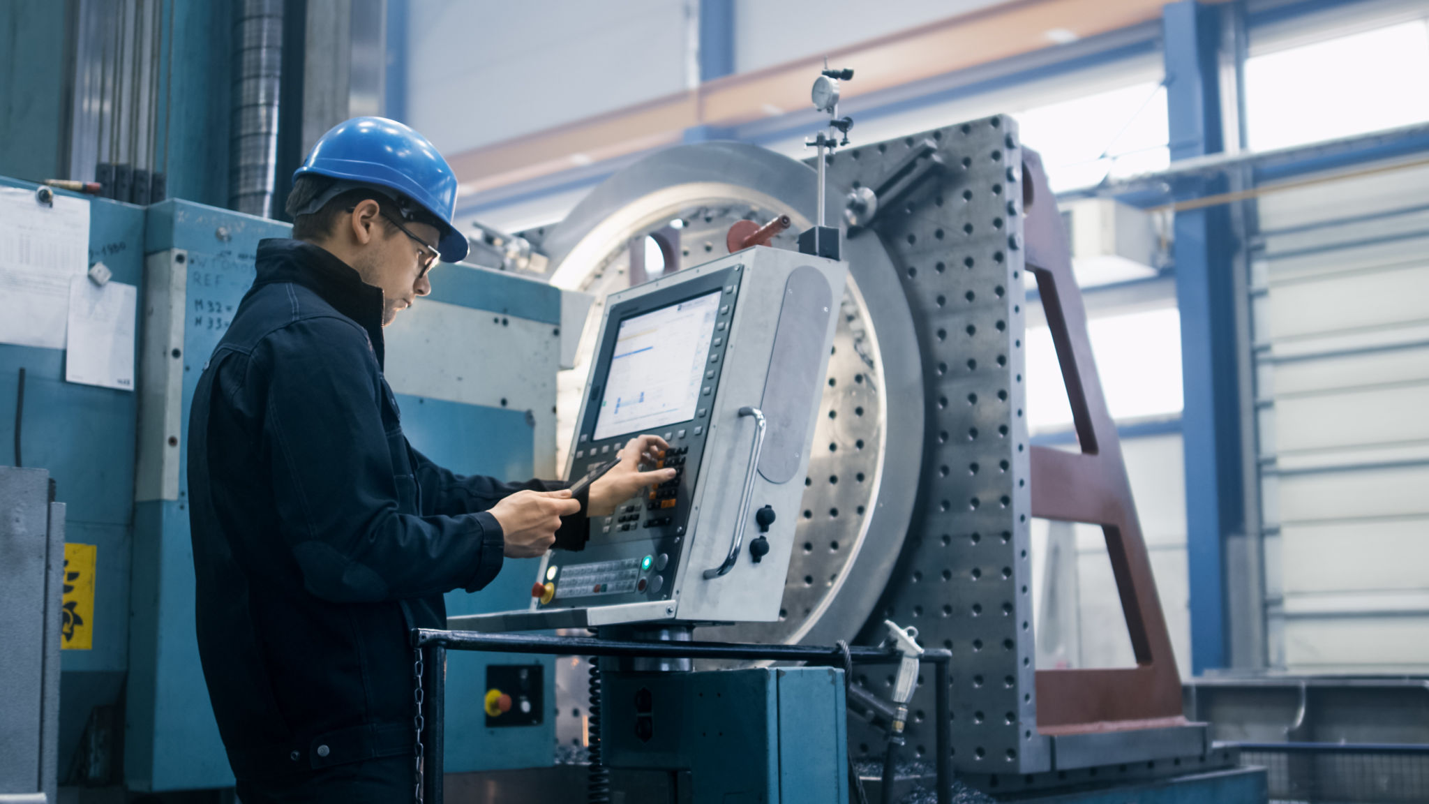Factory worker is programming a CNC milling machine with a tablet computer. Factory worker is programming a CNC milling machine with a tablet computer.