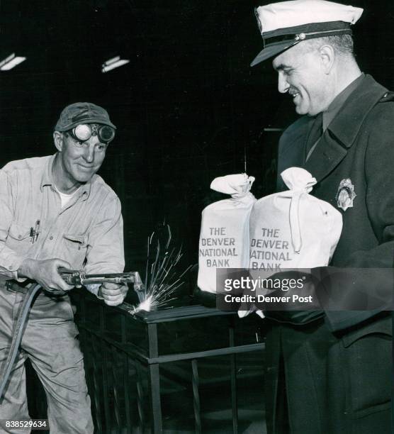 Officer George Curnow holds $38,000 as it is transferred to new Denver U.S. National Bank. Welder Jess Shuler watches the bags as he uses cutting...