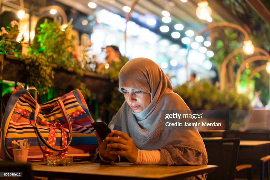 Muslim woman sitting alone using phone