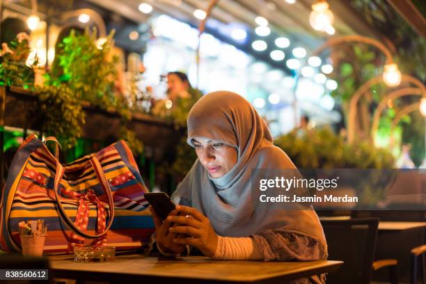 muslim woman sitting alone using phone - turco de oriente medio fotografías e imágenes de stock