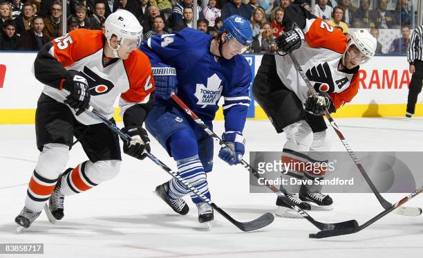 Matt Stajan of the Toronto Maple Leafs carries the puck as he skates through Simon Gagne and Matt Carle both of the Philadelphia Flyers during their...