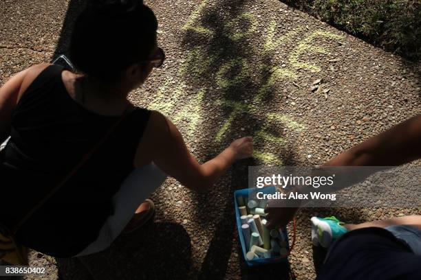 Protester writes a slogan with a piece of chalk on the sidewalk during a rally calling on the removal of a Confederate soldier statue on the grounds...