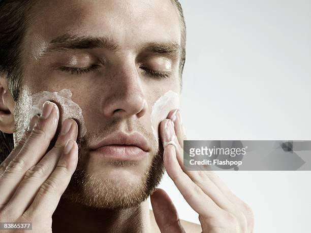 portrait of man applying moisturizer to face - creme rosto imagens e fotografias de stock
