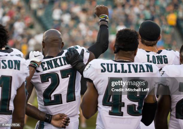 Malcolm Jenkins of the Philadelphia Eagles holds his fist in the air while Tre Sullivan stands behind him and Chris Long puts his arm on his shoulder...