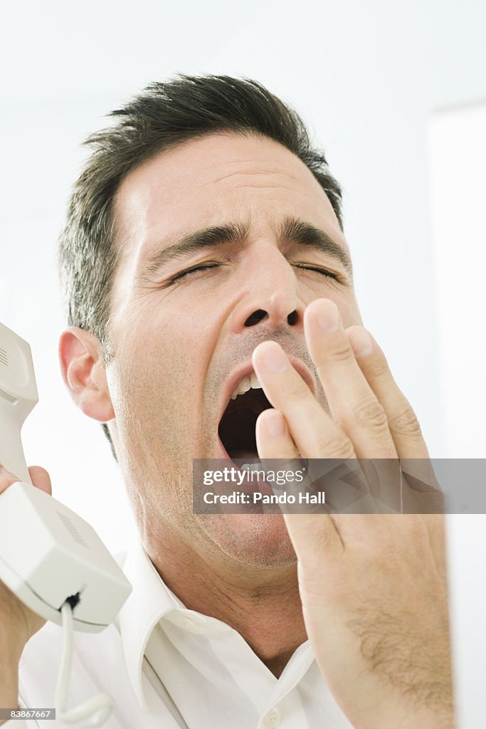 Man yawning while talking on the phone 