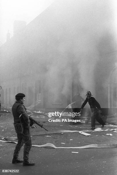 British soldier guards firemen fighting a blaze after a bomb blast at a miller's beside the River Foyle in Londonderry, when bombers opened a new...